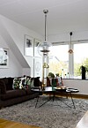 En bumlinglampa i mässing skapar härlig retrokänsla i vardagsrummet. I fåtölj och soffa ligger kuddar med mönster av Josef Frank för Svenskt Tenn.