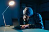 Hackare, bedragare framför dator med telefon i handen.