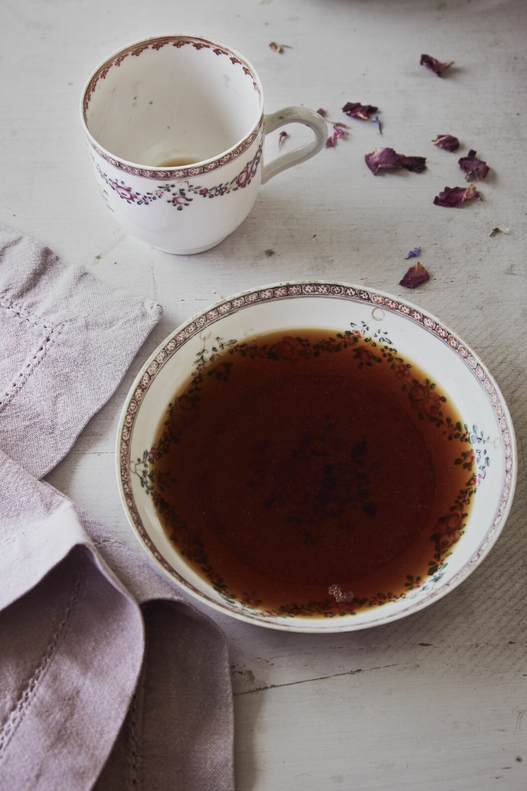 Traditionen att dricka på fat spreds under 1700-talet och levde kvar på landsbygden till långt in på 1900-talet. Kaffekopp med blommönster och ett kaffefat med kaffe på ett bord, med blomblad och servett bredvid.