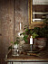 En ljusstake med levande ljus i, en glaskafaff och ett glas vatten, brun vägg och mässingsspegel i bakgrunden.