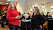 Två kvinnor står och pratar i ett café. Ena kvinnan har en röd tröja på sig.