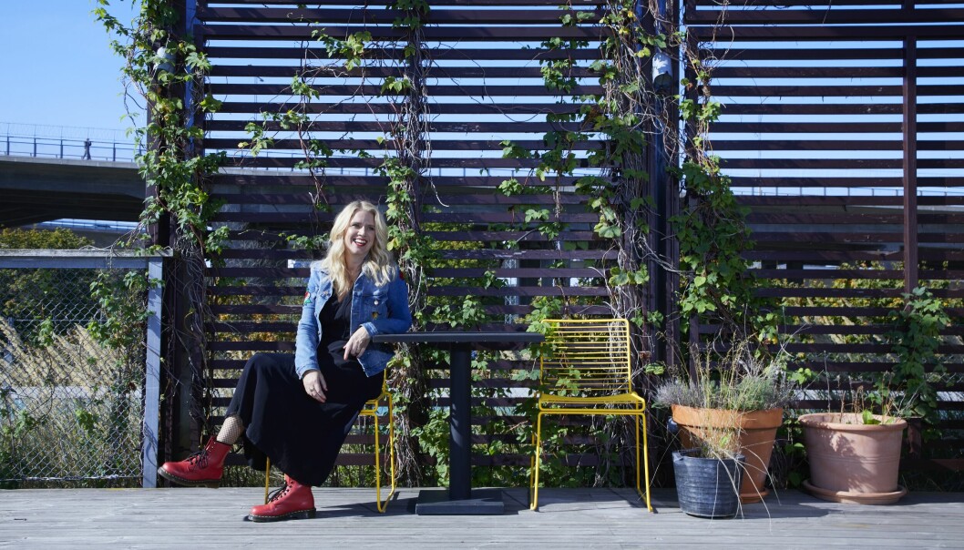Författaren Sofie Weidemann sitter i jeansjacka på en terass med krukor och spaljé, ler.