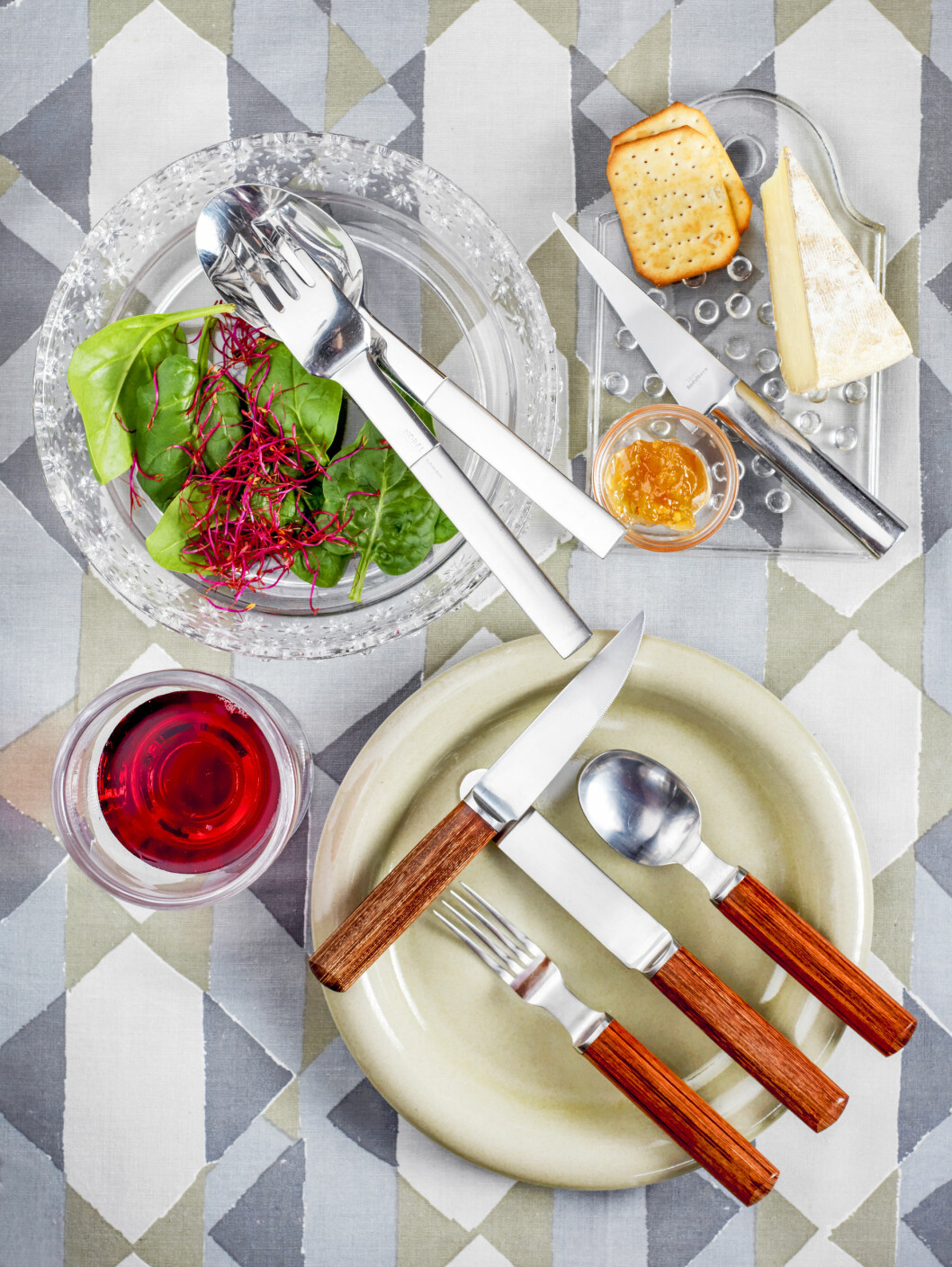 Det ganska sällsynta 1970-talsbesticket av Signe Persson-Melin med skaft av packawood och blad som smitts för hand i Danmark kompletterar servisen <span class=" italic" data-lab-italic_desktop="italic">Boda Nova</span> av samma formgivare. Ostkniven <span class=" italic" data-lab-italic_desktop="italic">Oval Steel</span> från 1976 är formgiven av Mikael Björnstjerna för Boda Nova-serien och uppläggningsbesticken av Gunnar Cyrén ingår i Nobelservisen 1991. På fat och skålar ligger silverbestick, sallad, ost och kex på en mönstrad duk i vitt, grått och beigt.