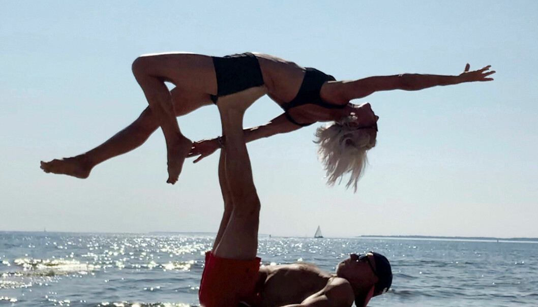 Det händer att Bia och Thomas stannar upp i sina utomhusaktiviteter för att utöva acroyoga. Som här under en varm dag i Luleå skärgård. Då får de ofta publik. Bia och Thomas gör yoga på en strand. Thomas håller upp Bias kropp med fötterna.