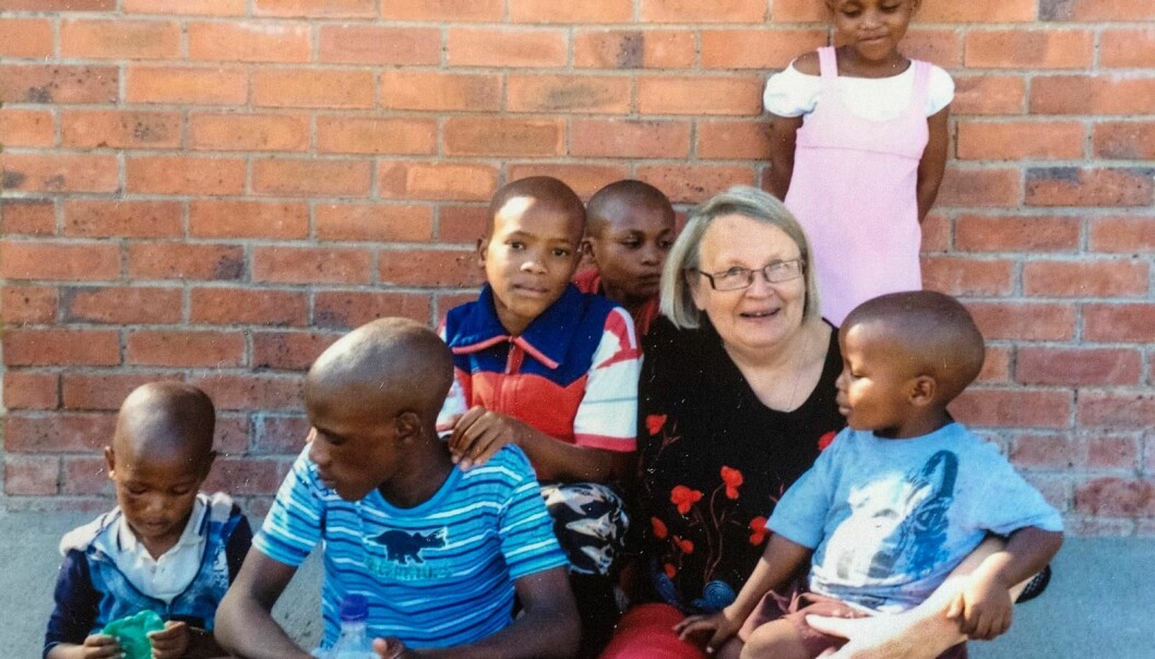 Birgitta har rest ner till barnhemmet i Lesotho flera gånger. Äldre kvinna, Birgitta, sitter med ett gäng barn runt sig, utanför barnhemmet.
