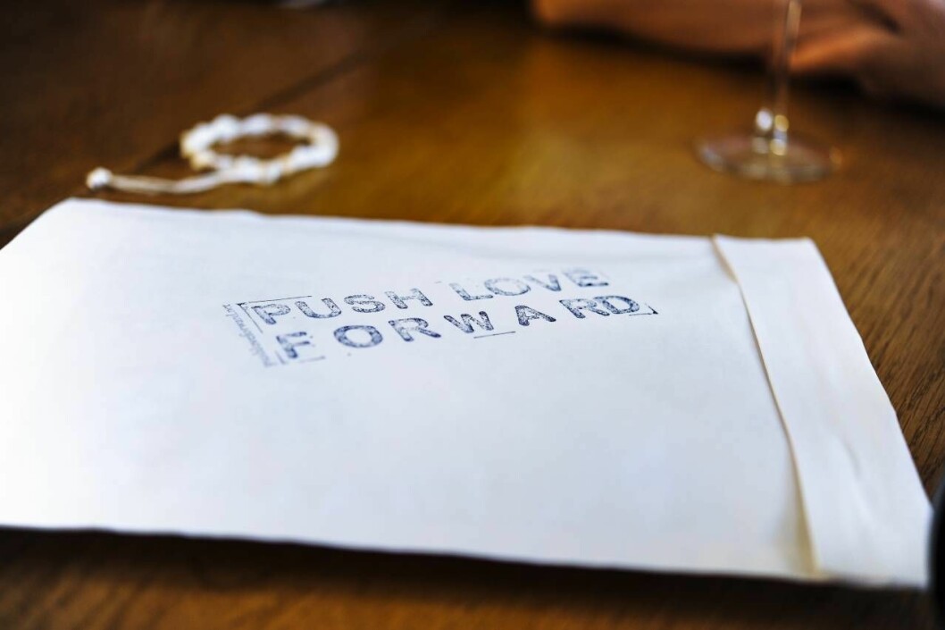Kassen innehåller bland annat ett armband med en pärla. Ett vitt kuvert med texten Push love forward på.