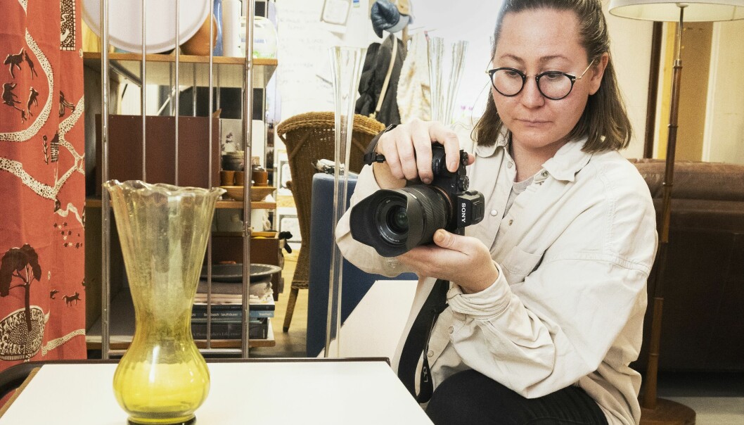 Amanda fotograferar en vas som står på ett bord och i bakgrunden syns möbler och föremål.
