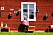 Anette sitter lutad mot ett rött hus och tittar in i kameran.