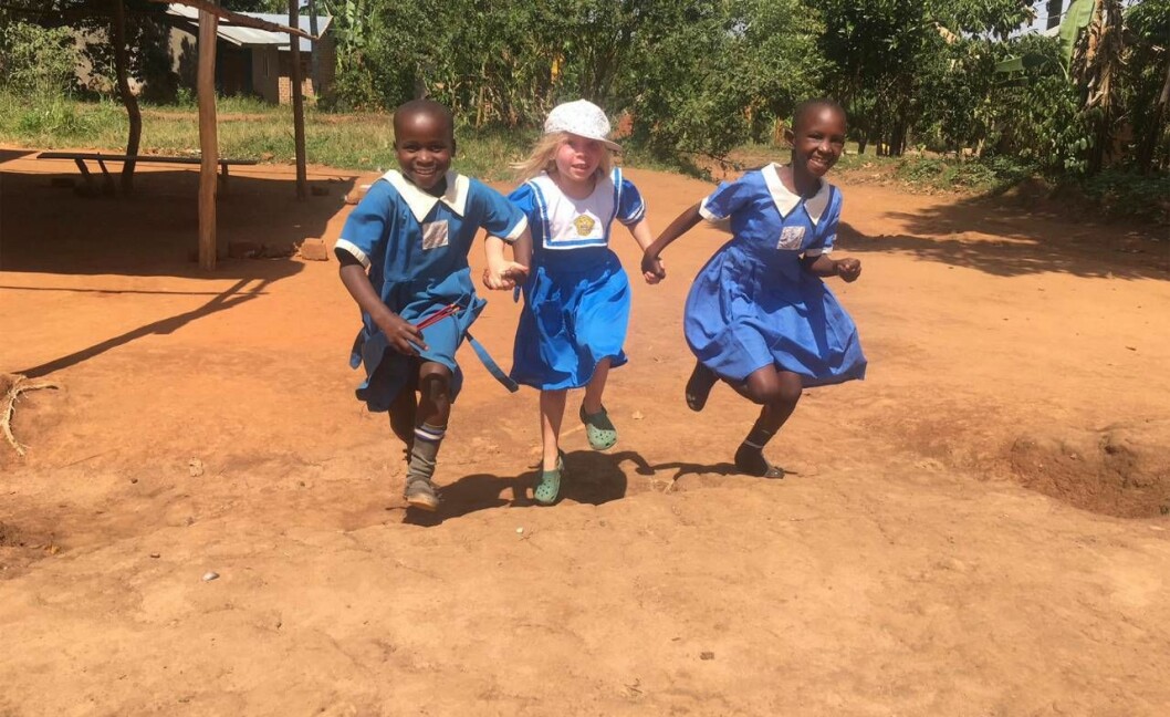 Ellen på språng med nya lekkamrater. Foto: Privat Tre barn springer hand i hand i en by i Uganda.