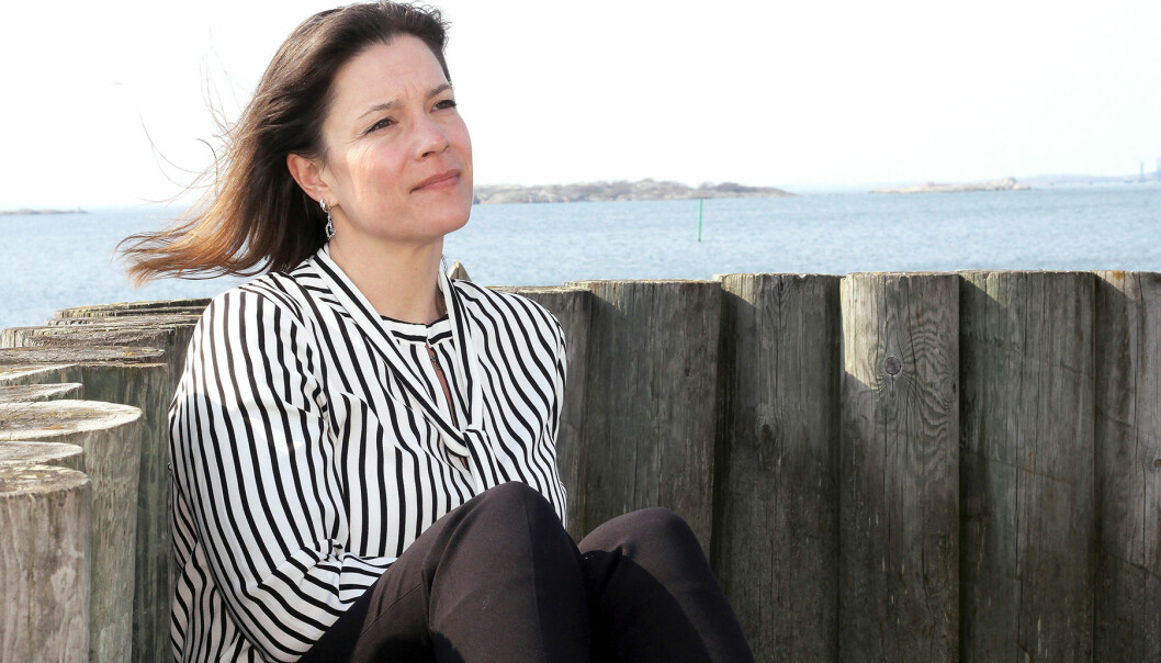 Anne-Liv sitter mot en trämur med havet i bakgrunden