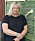 Anneli Magnusson står lutad mot en grön stalldörr med ett gult handtag fastskruvat. Hon är kladd i svart t-shirt och håller handen över ena armen. Hon har ljust axellångt hår och glasögon.