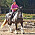 Annelie rider en svart vit häst. Hon har på sig ridhjälm och rosa t-shirt.