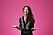 Nya programledaren för Melodikrysset Annika Jankell slår ut med händerna och ler glatt, där hon står iförd svarta kläder mot rosa bakgrund.