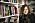 En kvinna med scarf står lutad mot en bokhylla i ett bibliotek.
