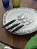 Sked, kniv och gaffel med svarta skaft på två vita talstallrikar med grått trekantsmönster i kanten.