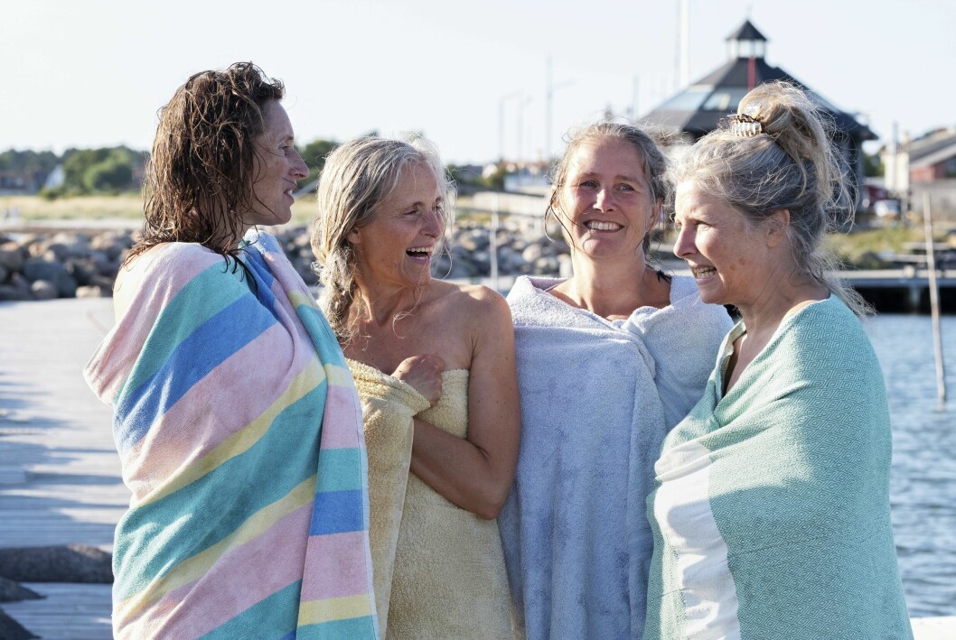 Fyra medlemmar av badklubben står och småpratar efter badet, invirade i handdukar.