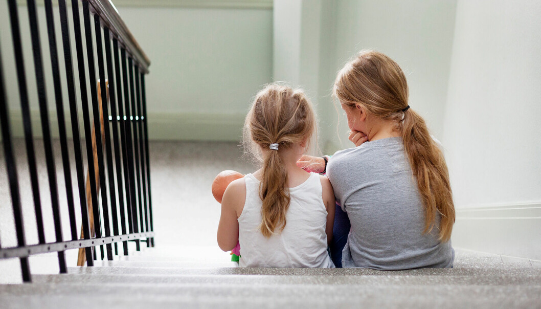 Två små flickor sitter i ett trapphus med sina ryggar mot kameran.