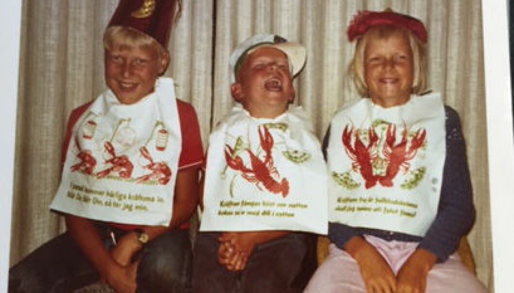En glad Janne mellan storebror Uffe och storasyster Bodil. Han har alltid gillat skaldjur och kräftor. Barnbild på storskrattande Janne mellan två syskon, alla med stora kräfthaklappar.