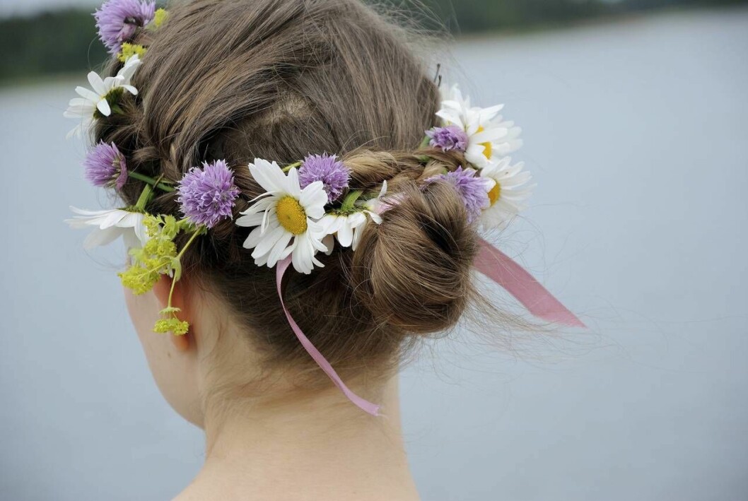 Fläta in blommor i håret för en fin festfrisyr med sommarkänsla. Kvinna i fläta med blommor