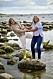 Birgitta Hågemark Olshov och Annika Erlandsson Olshov håller varandra i händerna där de leende står och balanserar tillsammans på en stor sten i vattnet nära strandkanten i Viken vid Öresund.
