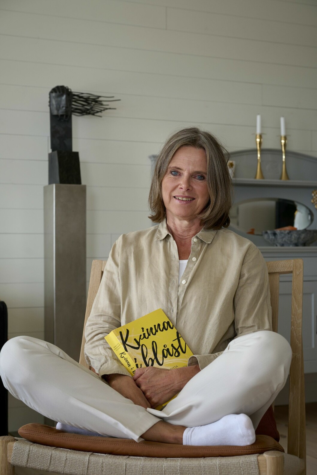 Birgitta Hågemark Olshov sitter på en stol med sin bok "Kvinna i blåst" i knät.