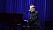 Björn Skifs sitter vid ett piano som han spelar på och samtidigt sjunger i en mikrofon. Han är klädd i en glänsande svart kavaj.