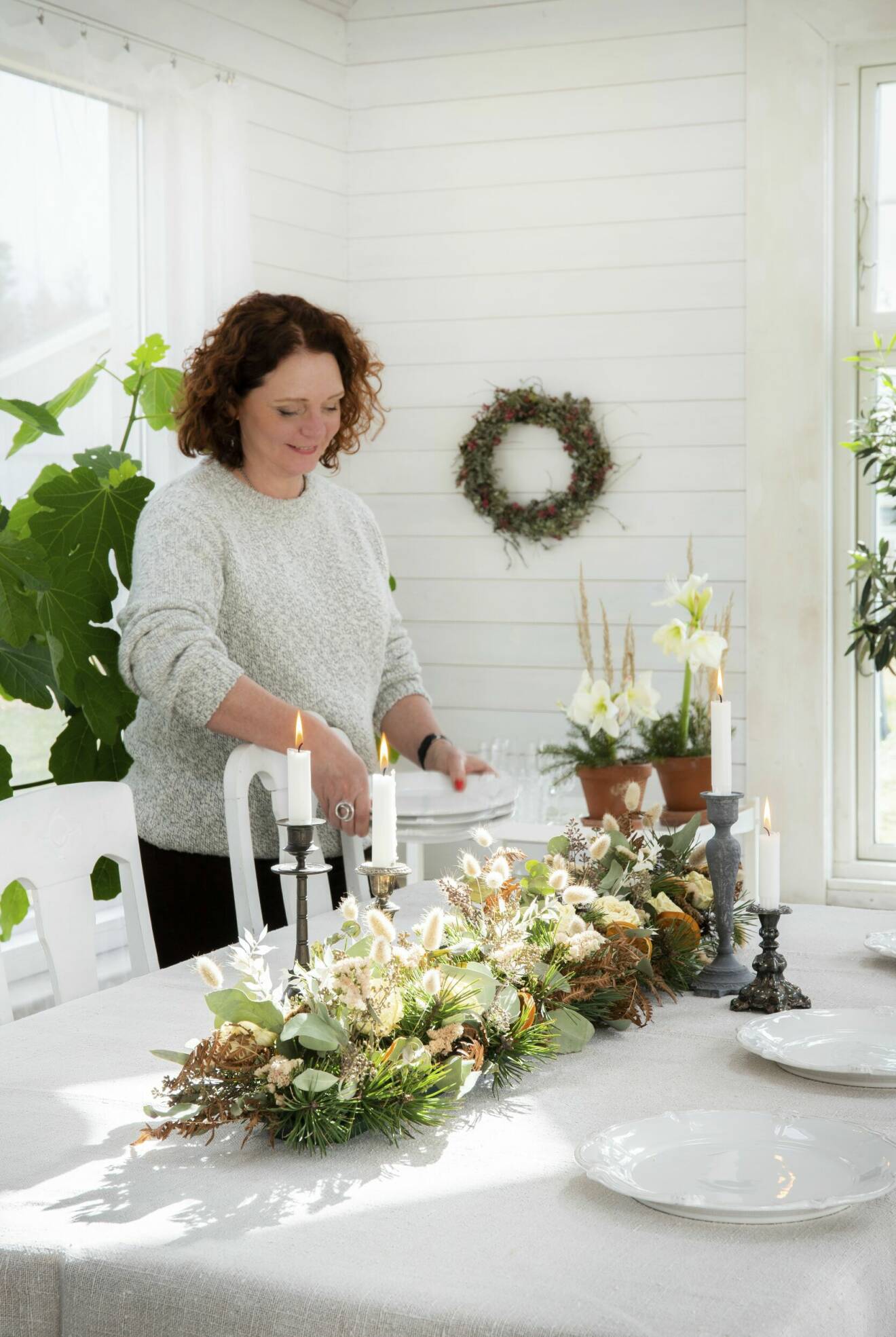 En kvinna dukar ett bord med en bordsdekoration av torkade blommor och växter.