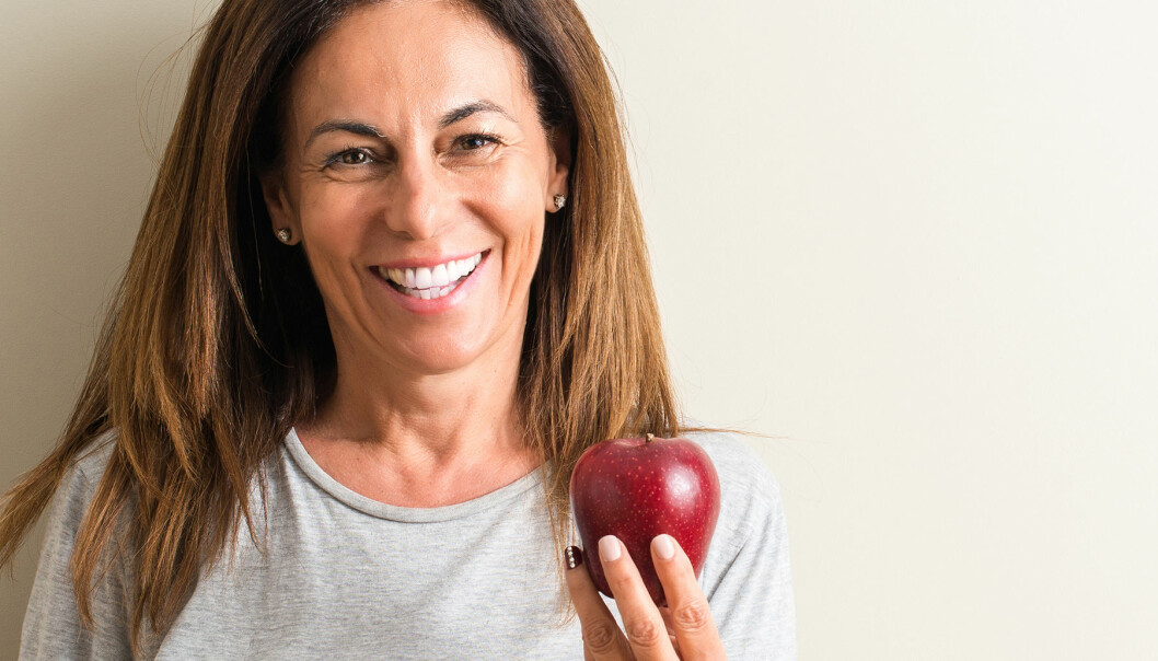Kvinna ler och håller upp ett äpple mot kameran