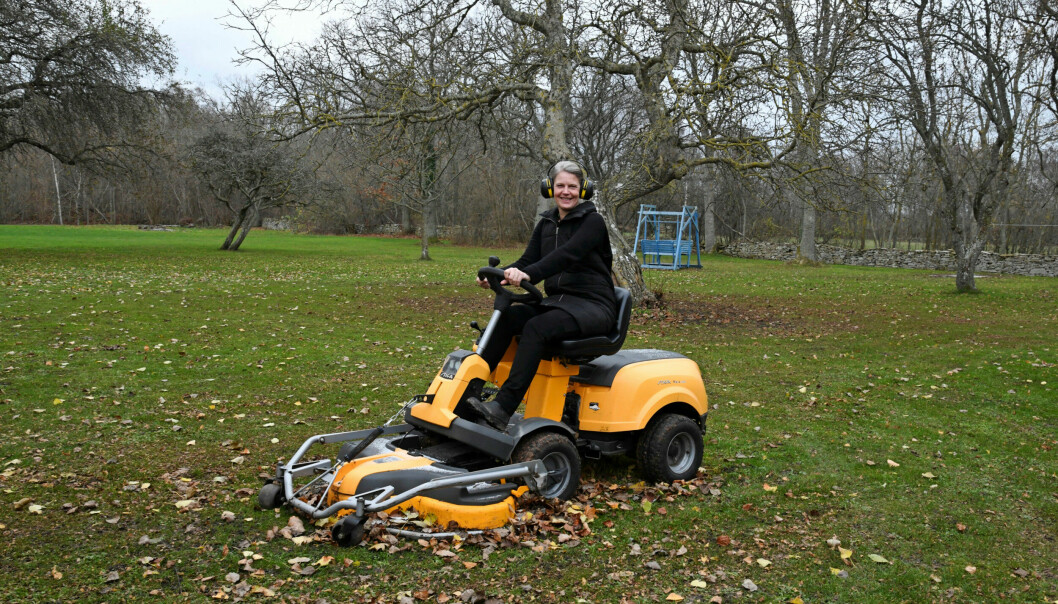 Cecilia sitter på en orange svart gräsklippare ute i trädgården.