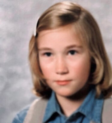 Christina blev mobbad för att hon var blind under en stor del av skolåren. Christina har välkammat axellångt hår, sidbena och en vit klämma håller håret borta från ansiktet, blå skjorta och beige väst och ser allvarlig ut.