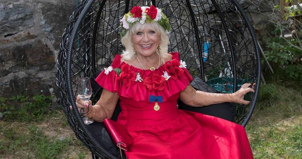 På sin 80-årsfest bar Christina Schollin samma klänning som hon hade på sin 50-årsfest, något redesignad. Foto: Charles Hammasten Christina Schollin i röd klänning och blomsterkrans.