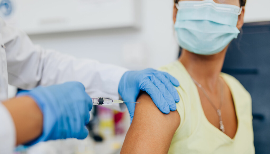Kvinna med munskydd får vaccin genom en spruta i armen.