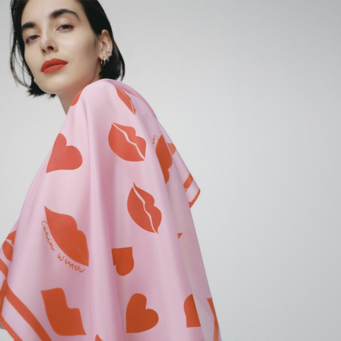 Tanken var att designa en scarf som "poppar". Scarfen passar utmärkt till höstrocken eller som en färgglad detalj på handväskan. <a target="_blank" rel="nofollow" href="https://in.ahlens.se/t/t?a=1136856392&as=1219652846&t=2&tk=1&epi=js-brostcancer-scarf-rosa&url=https://www.ahlens.se/Mode/accessoarer/halsdukar-scarves-15213/carin-wester-scarf-heart-lips-onesize-pink-multi-61011587/">Klicka på bilden för att komma direkt till produkten!</a> Modell med scarfen designad av Carin Wester över axlarna. Scarfen är rosa med röda läppar och hjärtan på.