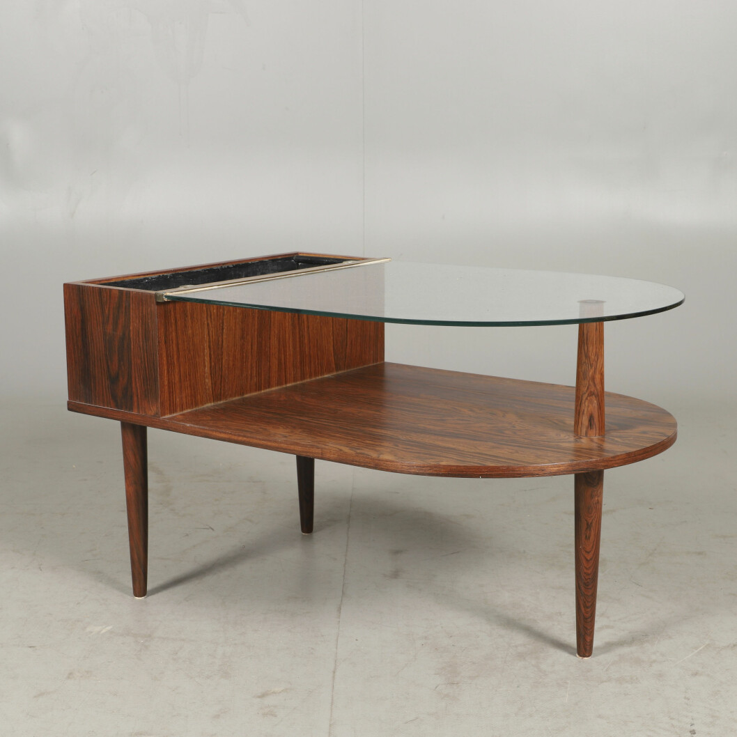 Dansk elegans med blomlåda och bord i ett. Materialen är jakaranda och glas, längden 85cm och höjden 50. Hos Helsingborgs Auktionskammare såldes möbeln som sig bör med ett CITES-intyg och värderingen låg på 1500 kronor. Tillverkningstiden är 1900-talets mitt. Blomsterbord och bord med glasskiva i ett, i materialet jakaranda.m