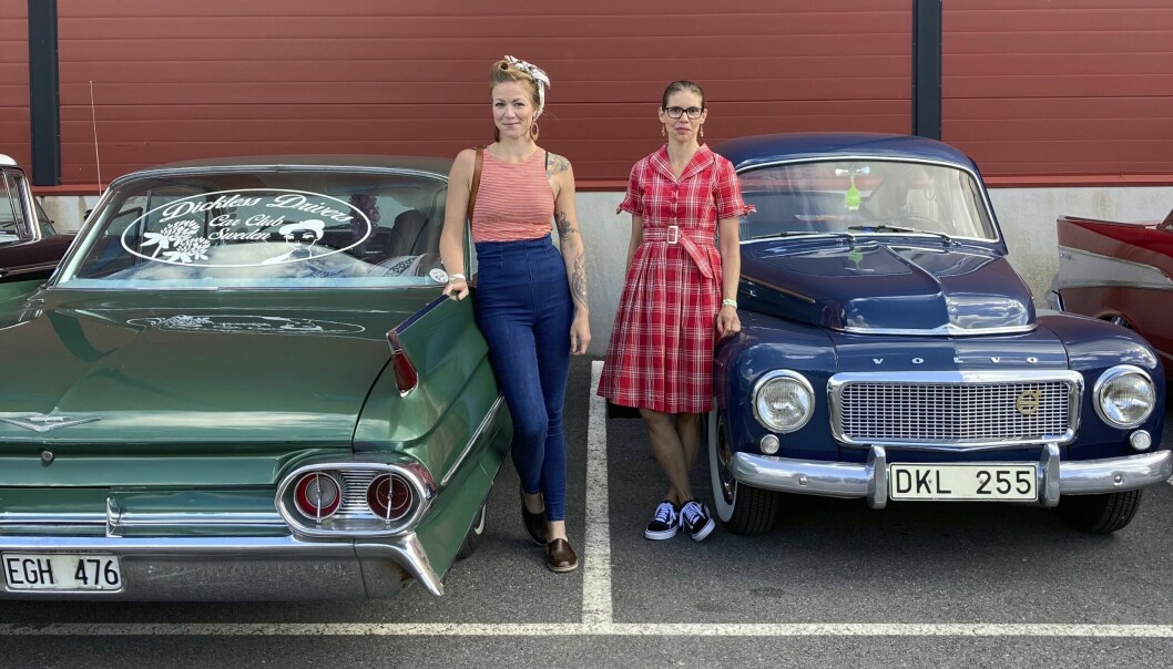 Julia Lind och Annelie Sundberg i retrokläder framför sina veteranbilar, en grön Cadillac coupé Deville och en blå Volvo PV.