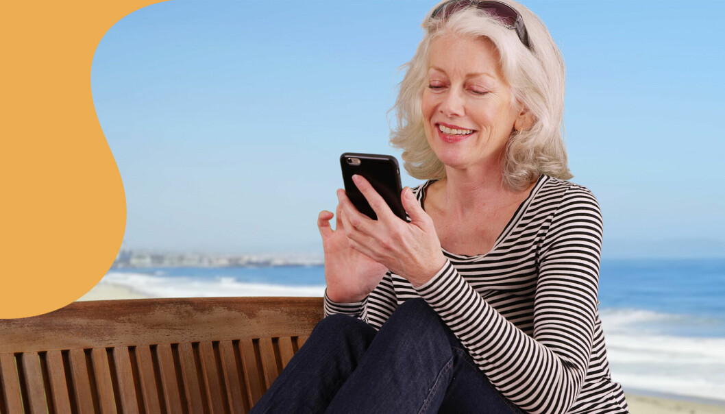 Bilden visar en kvinna på stranden som använder mobilen.