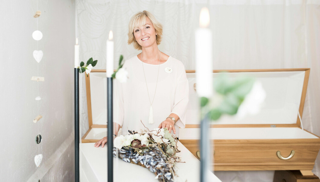 Dödsdoulan Jenny-Ann står vid en öppen kista och blommor och levande ljus runt.