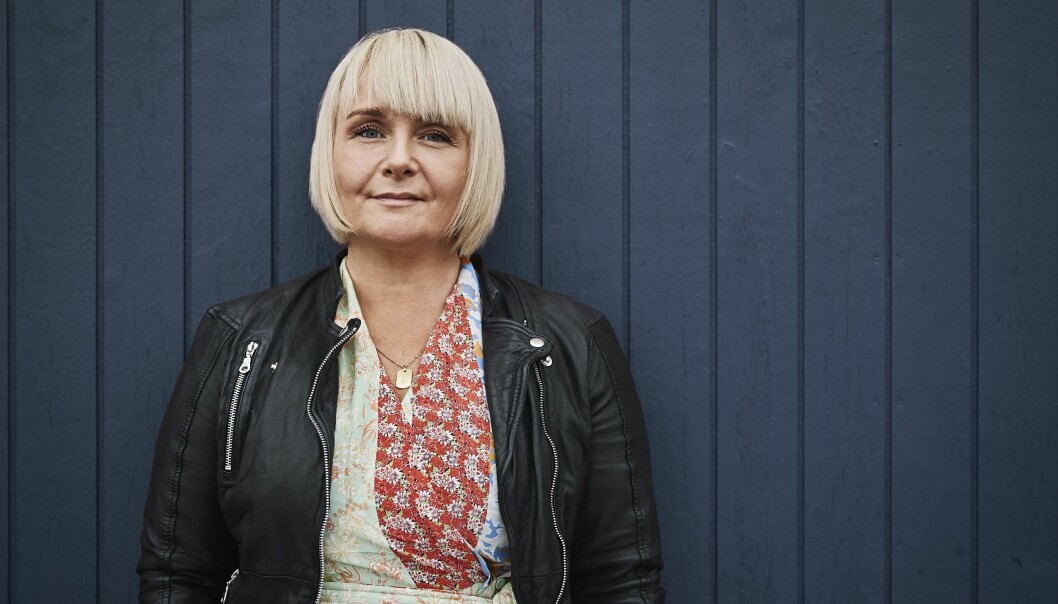 Arbetet som social- och sundhetsassistent kräver vanligtvis 18 tusen steg under ett pass, och även om Dorthe numera kan gå är det fler steg än hennes kropp klarar av. I stället drömmer hon om att bli doula, ett stöd för föderskan före, under och efter förlossningen. Foto: Runolfur Gudbjornsson Dorthe Bolther har blond page och en svart läderjacka. Hon lutar sig mot en mörkblå vägg och ser in i kameran.