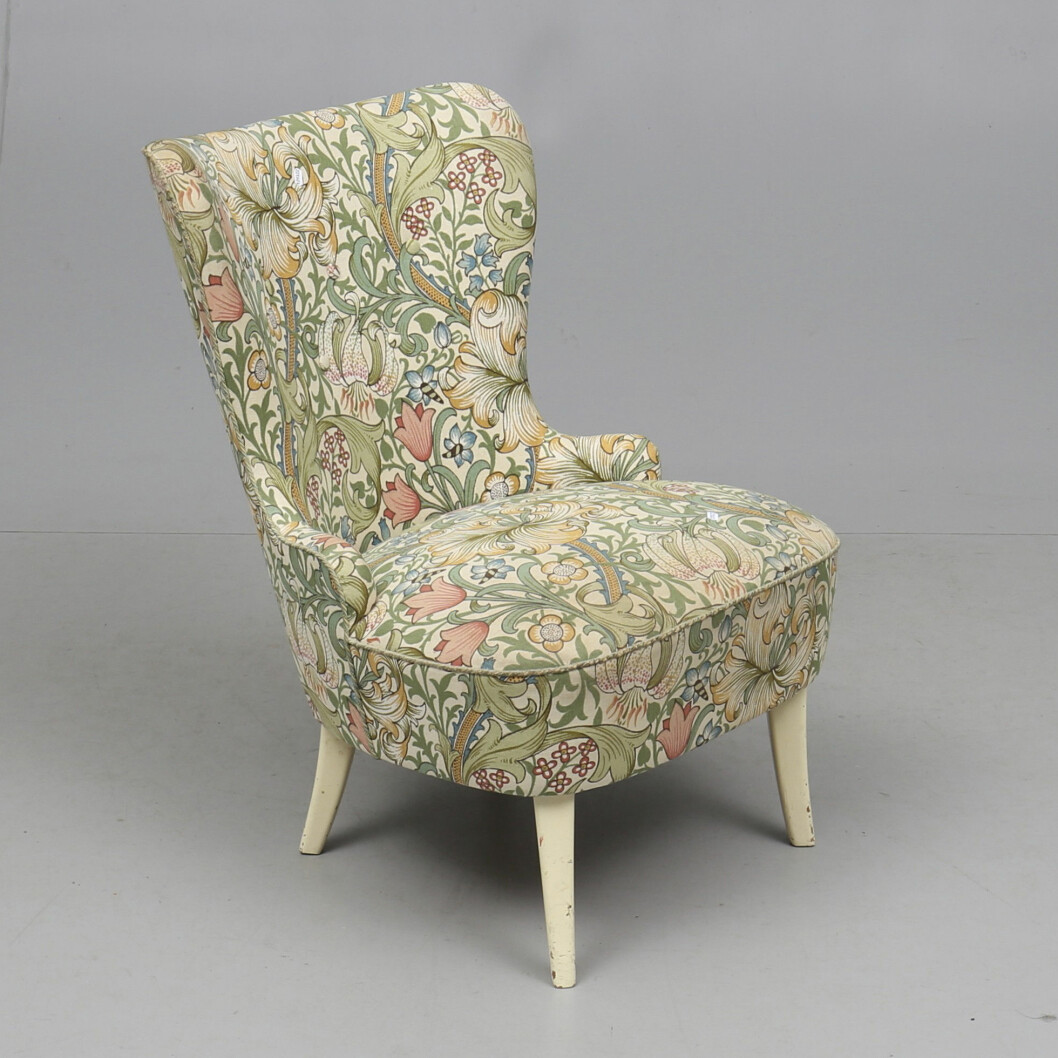 Emmafåtöljen från mitten av 1900-talet är klädd i en ljus variant av <span class=" italic" data-lab-italic_desktop="italic">Golden Lily</span>. På Auktionshuset Gomér & Andersson gav man den ett värde på 800 kronor 2018. Emmafåtölj klädd i tyg av mönstret Golden Lily av William Morris.