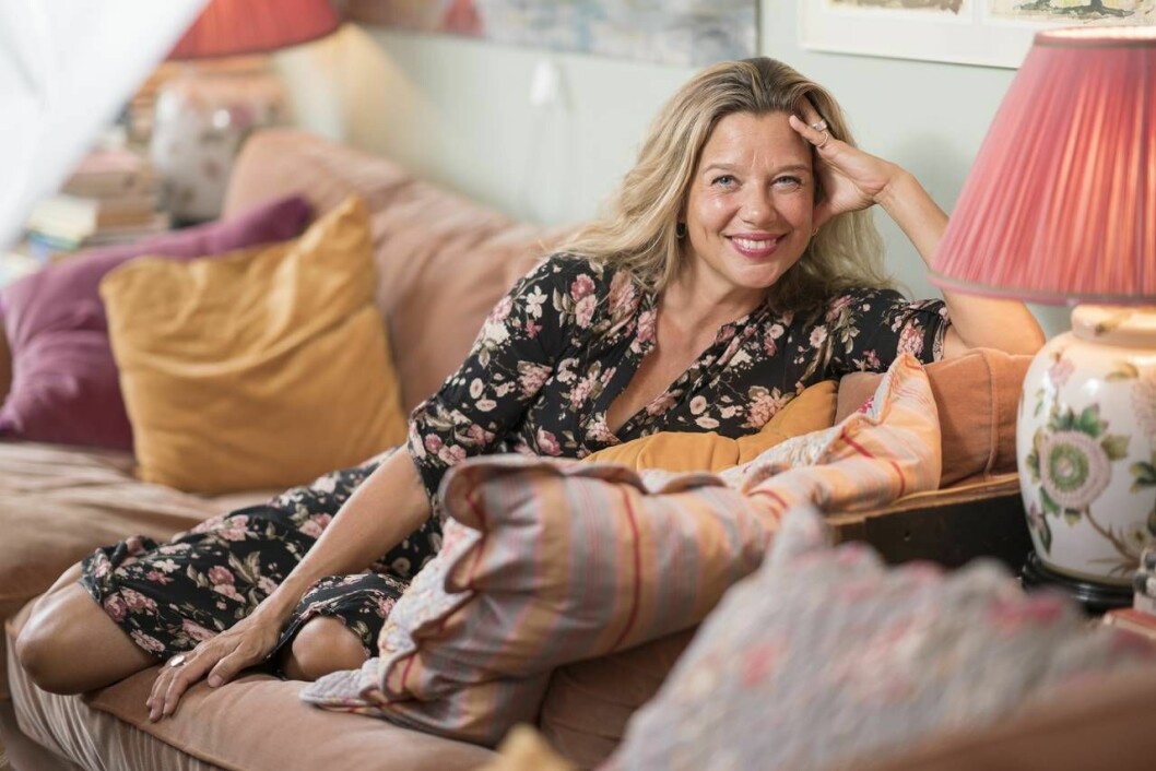 Emma Hamberg myser i soffan hemma i lägenheten som hon kallar ”matriarkatet ovan träden”. Här bor hon tillsammans med sina tre döttrar. Emma Hamberg sitter i en soffa och ler mot kameran