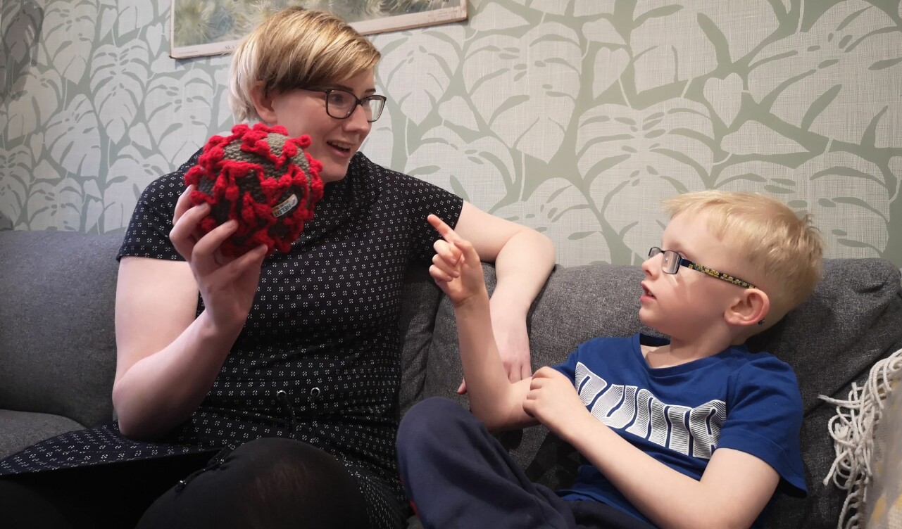 Emma Heldt sitter tillsammans med sonen Sixten i familjens soffa och visar upp sin hemvirkade coronaboll Virkus.