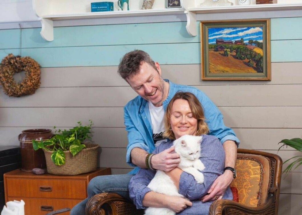 Emma och Arnold gläds åt sina husdjur, här med katten Fizzgig. Foto: Susanne Lindholm En kvinna i 45-årsåldern sitter med en katt i knät och hennes make bakom sig.