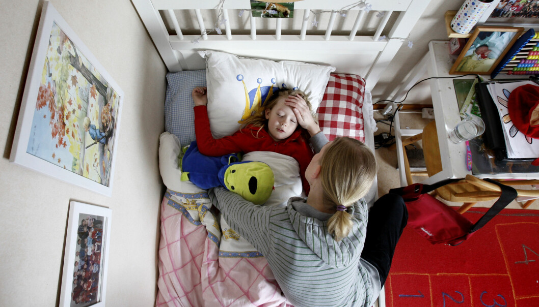 En kvinna håller handen på pannan på ett sjukt barn som ligger i sängen