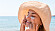 En kvinna i solhatt smörjer in ansiktet med solkräm.