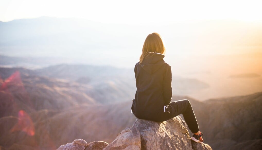 En kvinna sitter på ett berg i träningskläder och stressar ner.