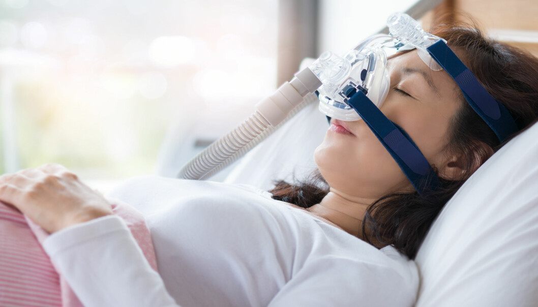 En kvinna sover i sin säng med CPAP-apparat.