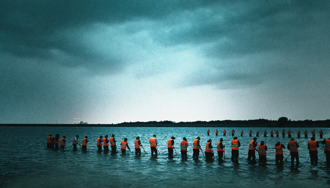 En scen ur tv-serien Utredningen, där en mängd människor med orange västar söker efter något i vattnet.