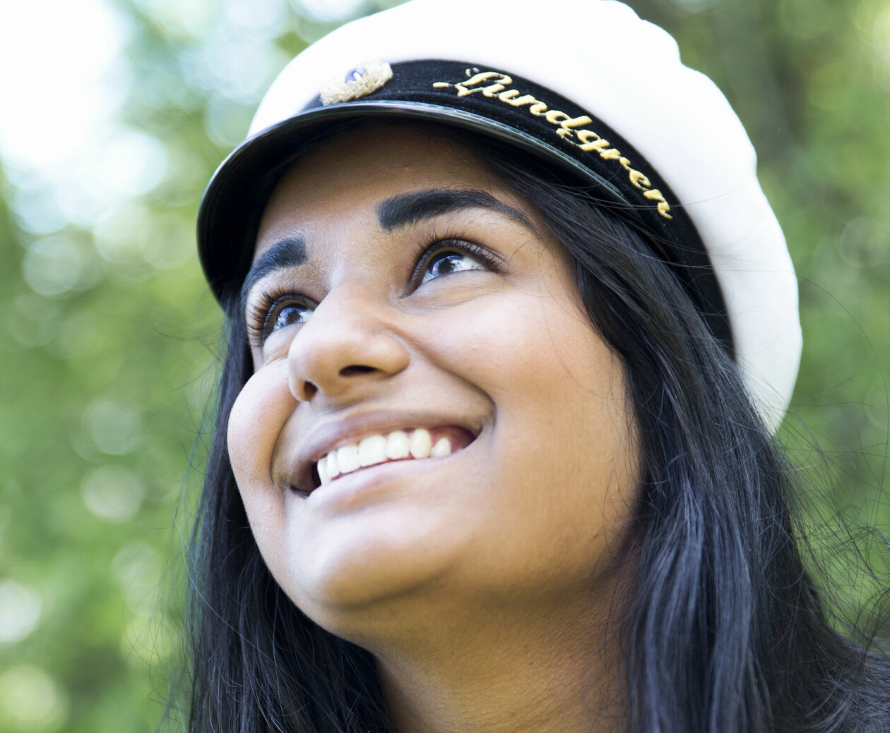 Visst går det att göra studentfirandet mer miljövänligt. Här får du tips på vägen. Foto: TT En studentska ler framför en grön, lummig bakgrund.