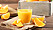 Ett glas med apelsinjuice och några apelsinklyftor på ett bord.