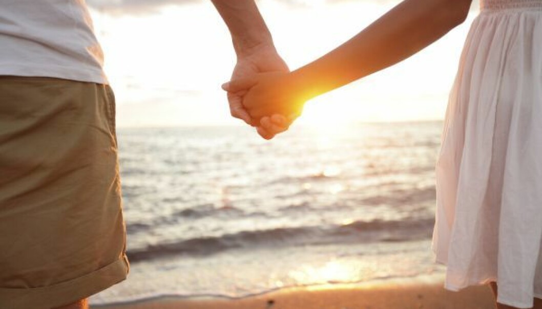 Sommar, solnedgång och romantik. Vad står skrivet i stjärnorna för din sommar? Foto: Shutterstock/TT Ett par håller varandra i händerna på en strand, i solnedgången.